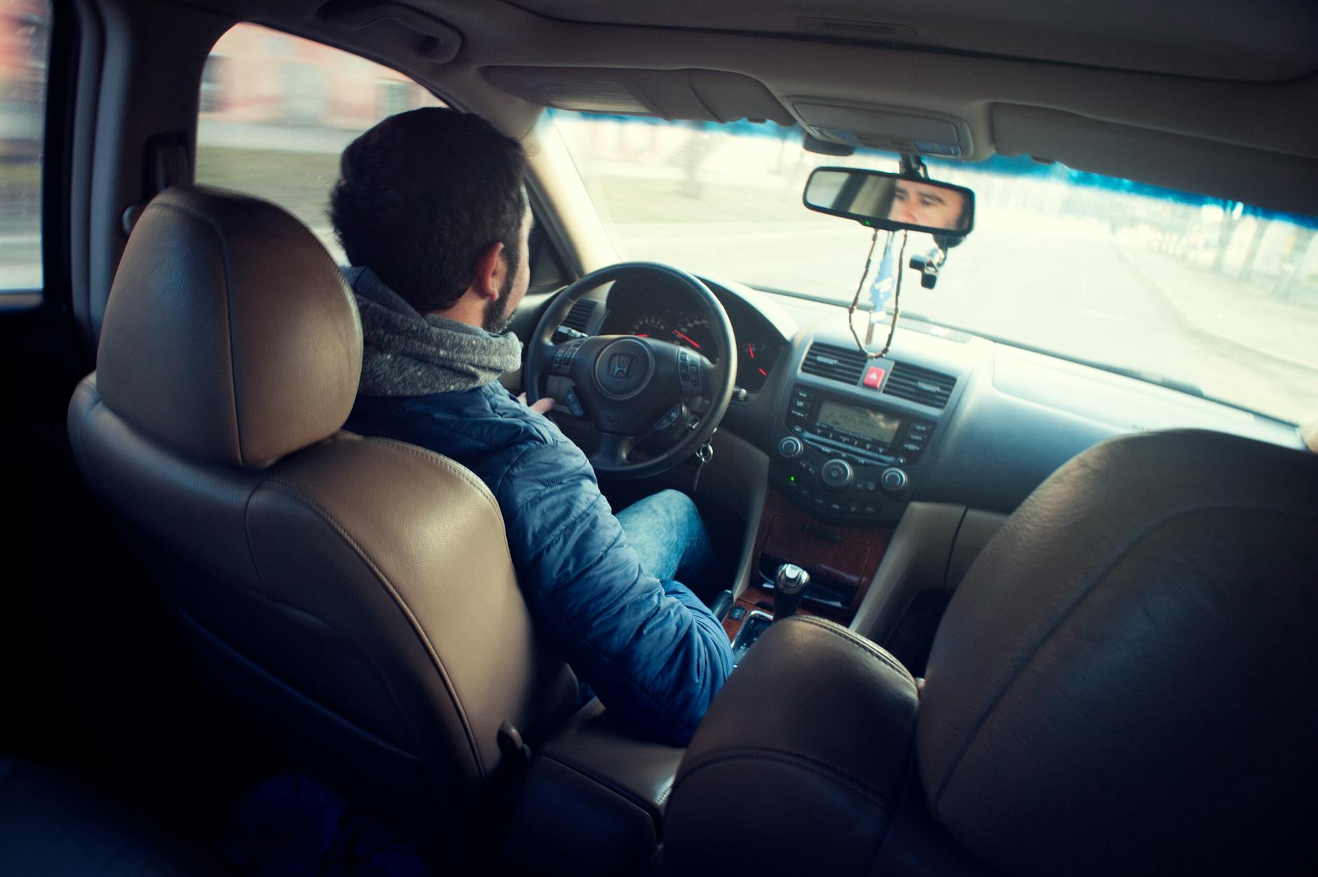 man wearing blue jacket sitting inside car while driving